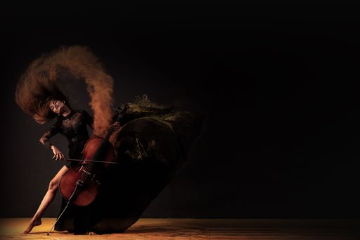 A dramatic photograph of a female cellist in motion, with her hair and dress creating dynamic shapes against a dark background.