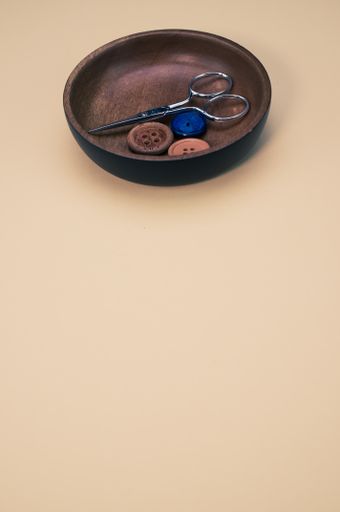 A vertical shot of scissors and buttons on a wooden bowl isolated on light brown background