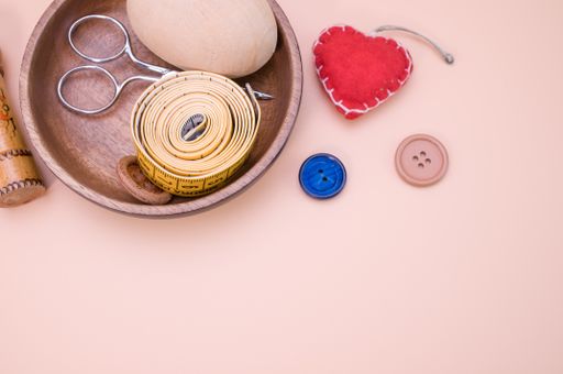 A top view of sewing materials on a wooden bowl isolated on light brown background