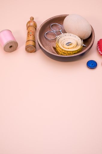 A vertical shot of sewing materials on a wooden bowl isolated on light brown background