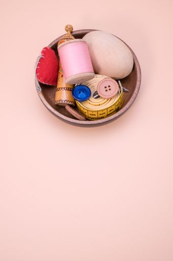 A vertical shot of sewing materials on a wooden bowl isolated on light brown background