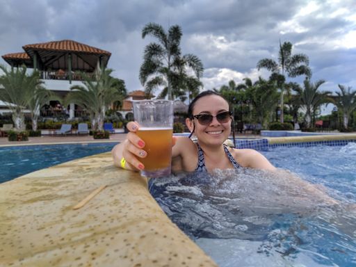 A pretty looking female with sunglasses in a pool holding a glass of beer