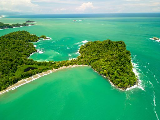 Aerial view of a tropical island with lush greenery and turquoise waters on a sunny day in Manuel Antonio beach, Costa Rica