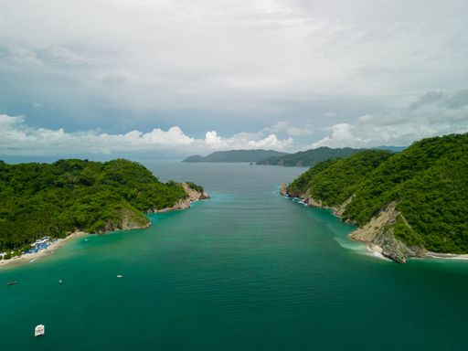Aerial view of a tropical bay with lush green hills and clear turquoise waters under a partly cloudy sky in Tortuga Island, Costa Rica