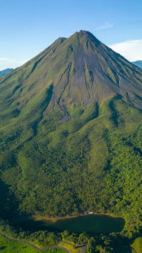 Aerial view of the Arenal Volcano in Costa Rica with lush green forest and clear blue sky