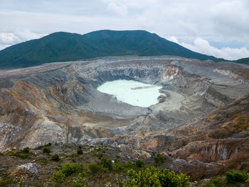 A breathtaking view of the Poas Volcano crater lake in Costa Rica, surrounded by rugged terrain and lush green hills under a cloudy sky.