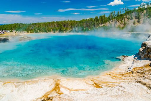A geyser erupting in Yellowstone National Park with steam rising against a clear blue sky