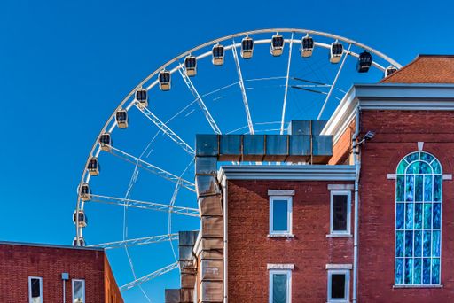 A closeup shot of a Ferris wheel near trees and buildings under a blue clear sky