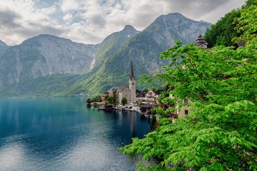 Beautiful view of Hallstatt village by the lake with mountains in the background and lush green trees in the foreground.