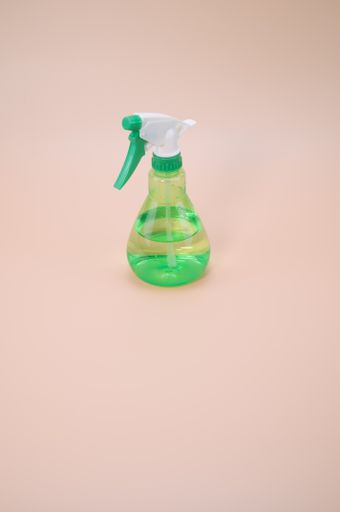 A vertical shot of green plastic sprayer isolated on light pink background