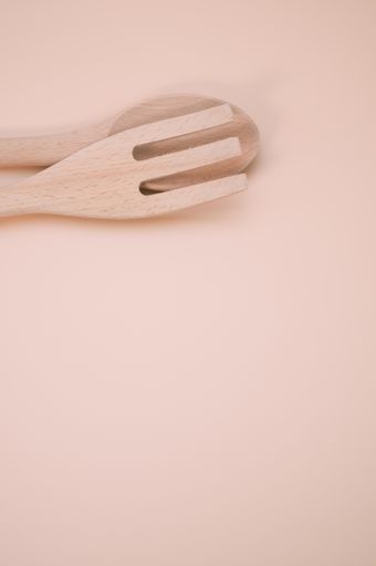 A vertical shot of wooden spoon and fork isolated on light pink background