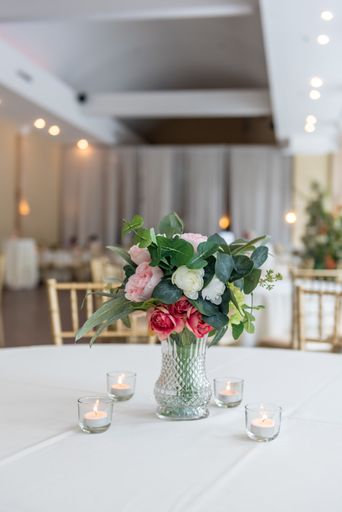 A vertical closeup shot of a flower bouquet in a glass vase on a white table with candles