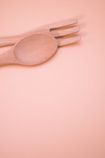 A vertical shot of wooden spoon and fork isolated on light pink background