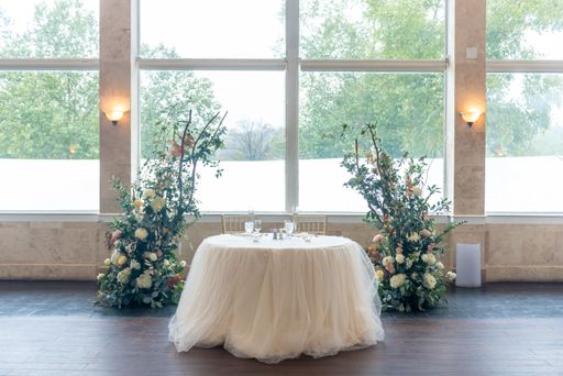 A beautiful table decorated with white fabric and flowers by the big windows
