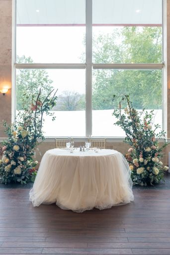A vertical shot of a small table with tulle and two floral compositions in the wedding hall