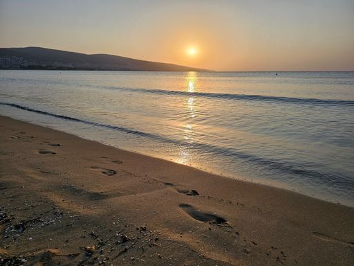 A beautiful sunset over a calm sea with footprints on a sandy beach. Bulgaria