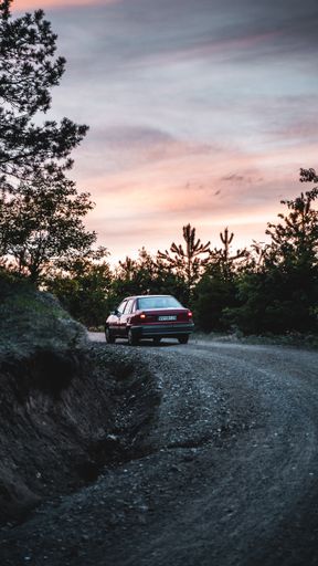 A vertical shot of a car driving through a winding road at sunset