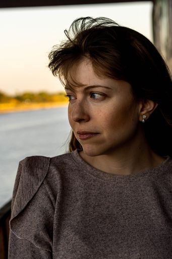 A vertical portrait shot of a Hispanic woman with her head tilted to the side looking out the window