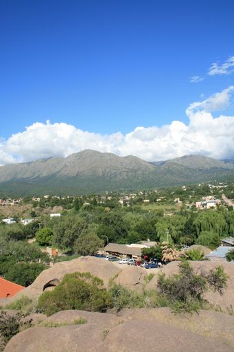 A Beautiful view of green forest and houses with dirt mountains on the horizon under blue cloudy sky