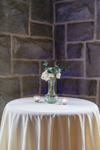 A vertical shot of a small vase with white roses on a small white table in front of a stone wall
