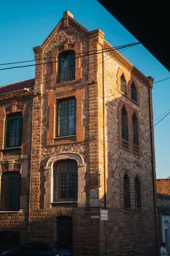 A historic stone building with brick accents and green windows under a clear blue sky in the evening light
