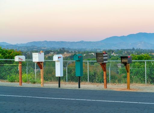 A row of mailboxes on the side of a street next to a fence during sunset under a clear gradient sky