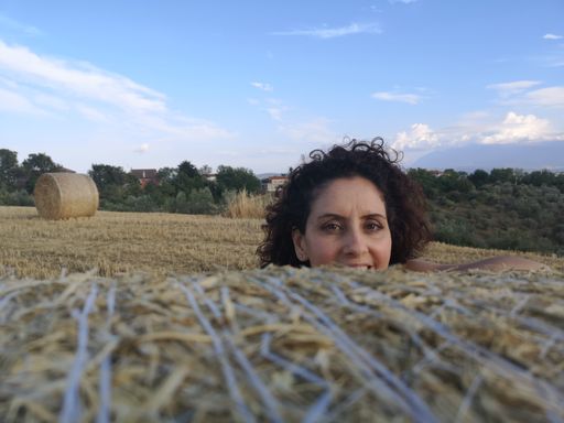 A young Italian female leaning against a round bale of straw