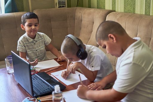 Three young male pupils drawing while listening to the online art class on a laptop at home