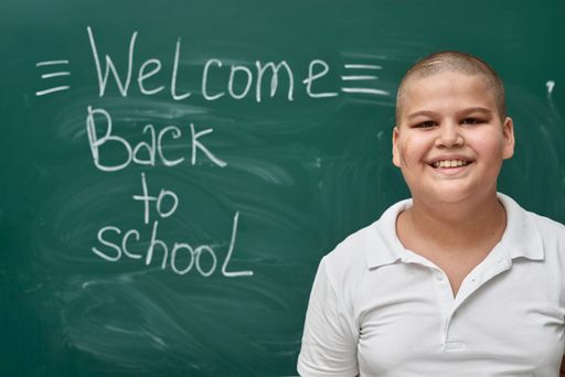 A young male pupil standing near the blackboard with "Welcome back to school" written on it