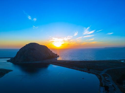 A stunning sunset view over Morro Rock at Morro Bay, California, with vibrant colors in the sky and reflections on the water.
