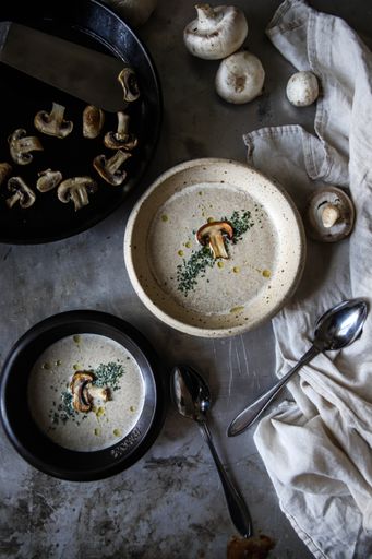 A top view of mushroom soup in white and black bowls on a gray table