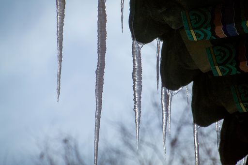 A low angle shot of thin icicles handing from the wavy patterned roof on a cold winter day