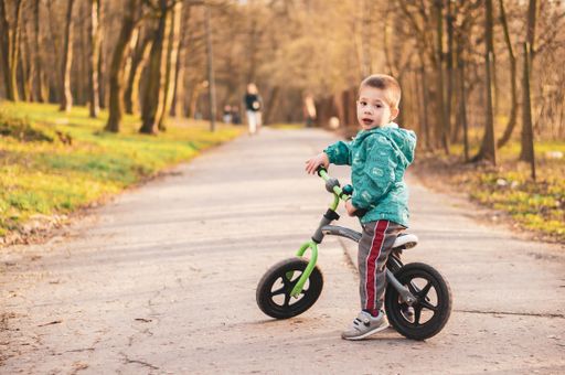 Young two years old Polish Caucasian boy sitting on a running bike on a footpath at a park.
