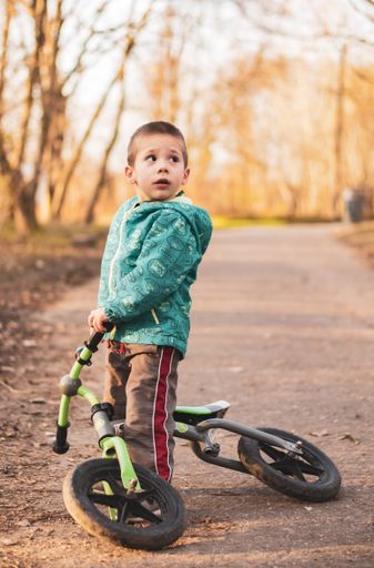 Small boy standing on a laying running bike on a footpath at a park.
