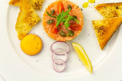 A top view of salmon tartare with avocado, egg and toast on a white plate