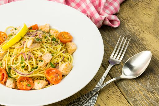 A closeup of creamy lemon salmon pasta on a white plate with cutlery on a wooden table