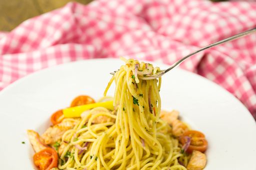 A closeup of creamy lemon salmon pasta on a white plate with a patterned towel