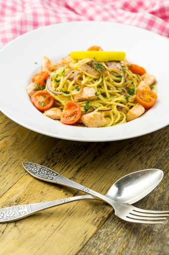 A vertical shot of creamy lemon salmon pasta on a white plate with cutlery on a wooden table