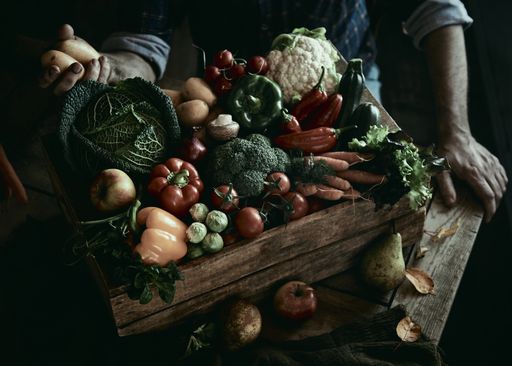 A high angle shot of crop male farmer sitting at the table with a wooden container full of various ripe fresh fruits and vegetables