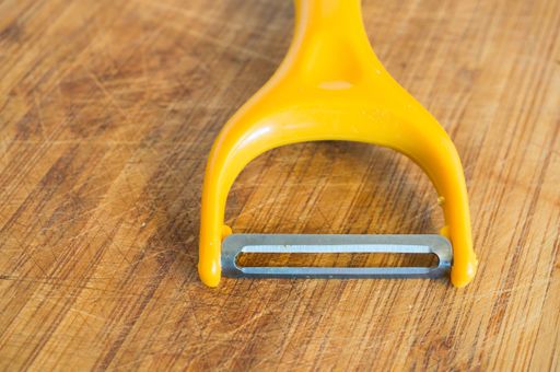 A yellow kitchen tool for peeling on the wooden surface with scratches