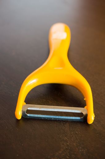 A closeup shot of a yellow fruit peeler on a wooden table