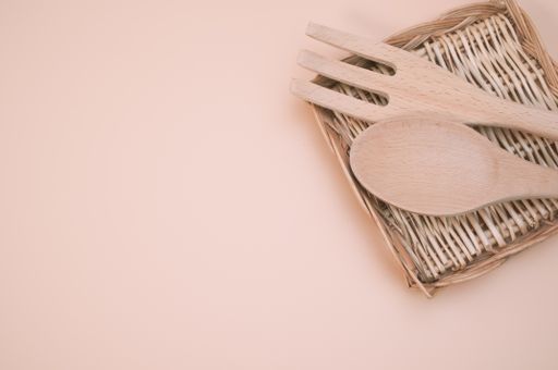 A top view of wooden spoon and fork on a flat wicker basket isolated on light cream background
