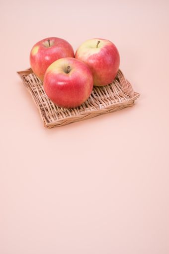 A vertical shot of apples on a flat wicker basket isolated on light cream background