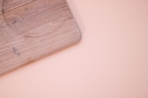 A top view of wooden chopping board isolated on light pink background with copy space