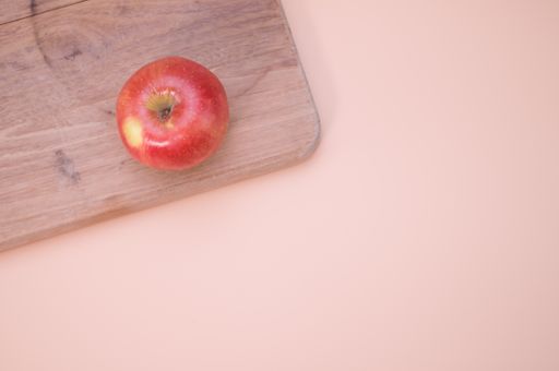 A top view of a red apple on a wooden chopping board isolated on light cream background