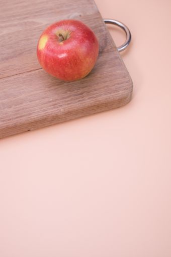 A vertical shot of a red apple on a wooden chopping board isolated on light pink background