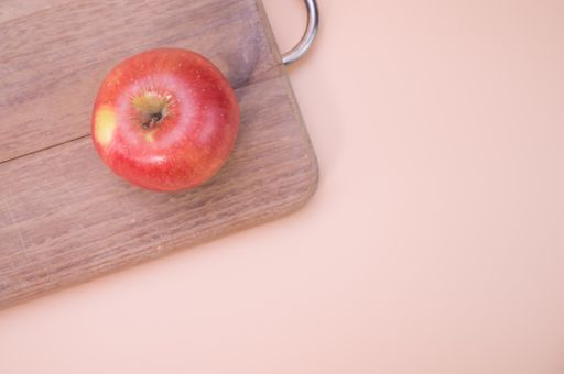 A top view of a red apple on a wooden chopping board isolated on light cream background