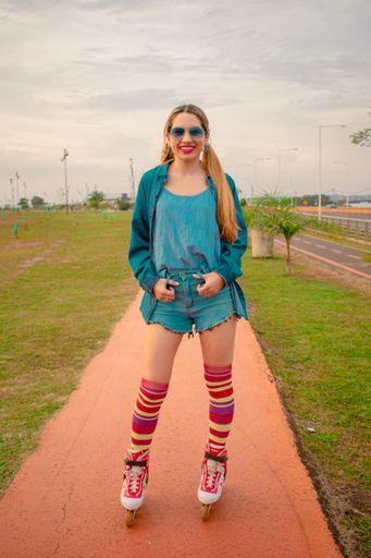 A vertical shot of a young Hispanic female in a retro roller skating outfit on a trail