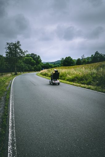 A vertical shot of an empty road in the countryside on a gray cloudy day with an elder driving on it on a toy car