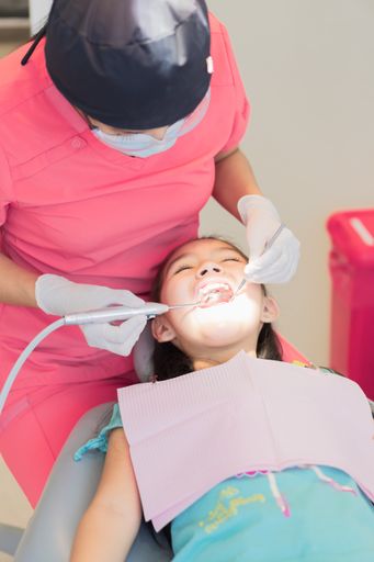 A vertical shot of a girl in a dental office, receiving dental treatment for the care of her teeth.